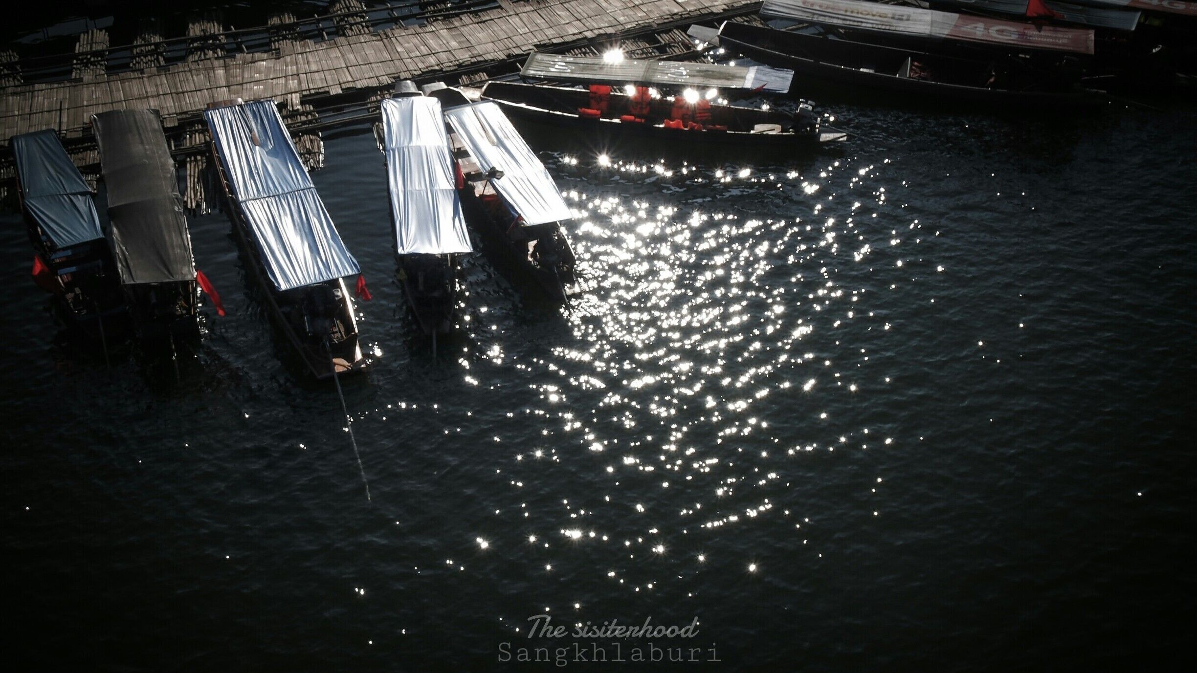 A nighttime view of a dock with boats and covered structures reflecting on the water.