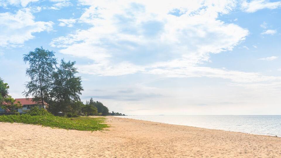 A wide sandy beach with calm water, a clear sky, and distant islands.