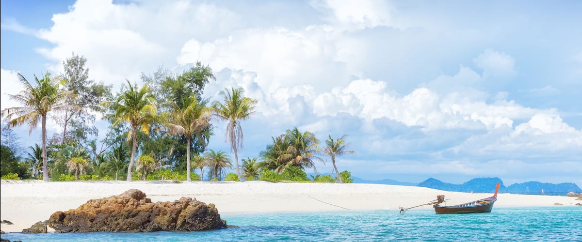 A beach with white sand, palm trees, and a boat in the water.