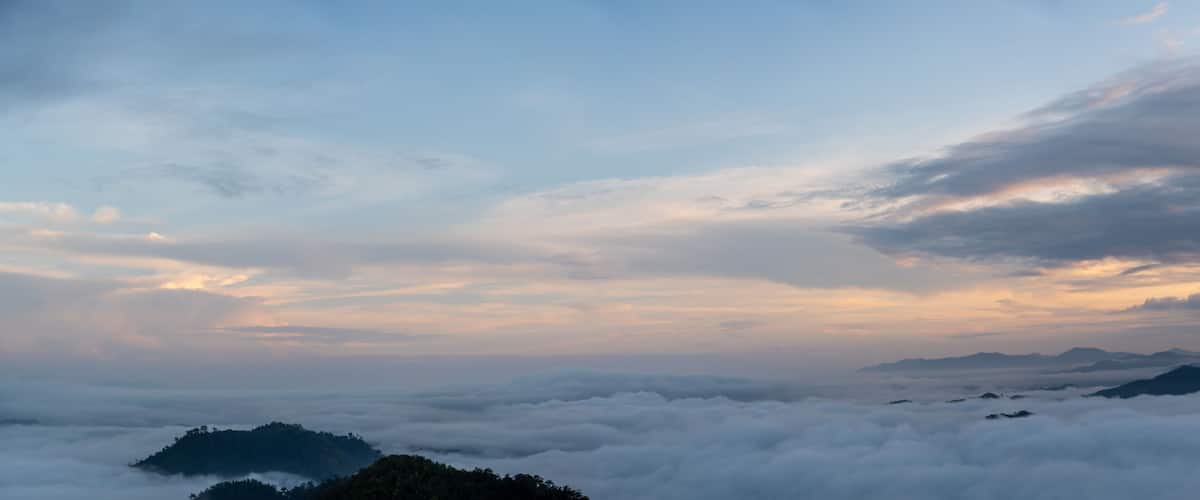 A mountainous landscape with clouds below the peaks and a partly cloudy sky.