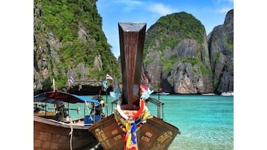 Een traditionele houten boot met kleurrijke versieringen afgemeerd aan een strand met helder turquoise water en rotsachtige kliffen op de achtergrond.