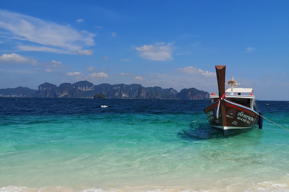 Ein Boot vor Anker in der Nähe eines Strandes mit klarem, türkisblauem Wasser und in der Ferne Bergen.