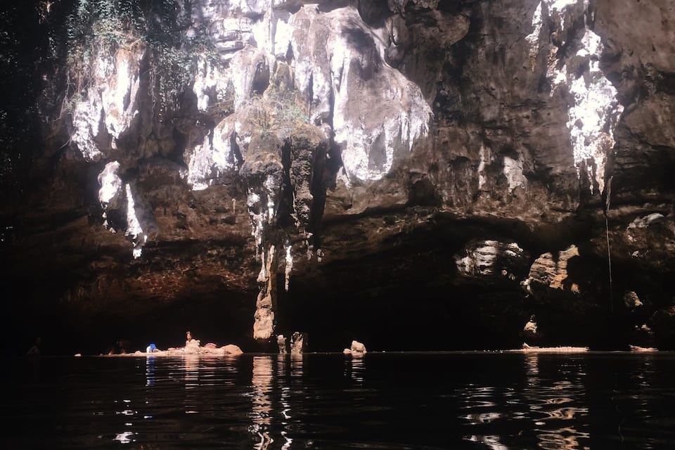 Una cueva con estalactitas colgando del techo y una masa de agua al frente.