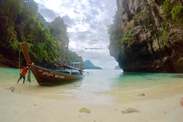 A boat named 'MAHMA' on a beach with clear turquoise water and rocky cliffs.