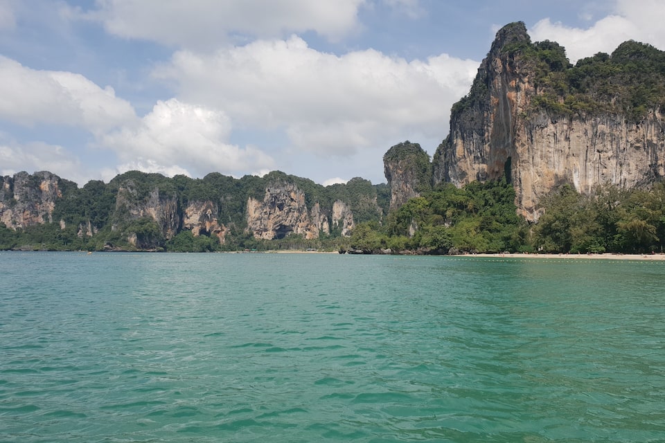 A coastal landscape with clear turquoise waters, a sandy beach, and towering limestone cliffs.