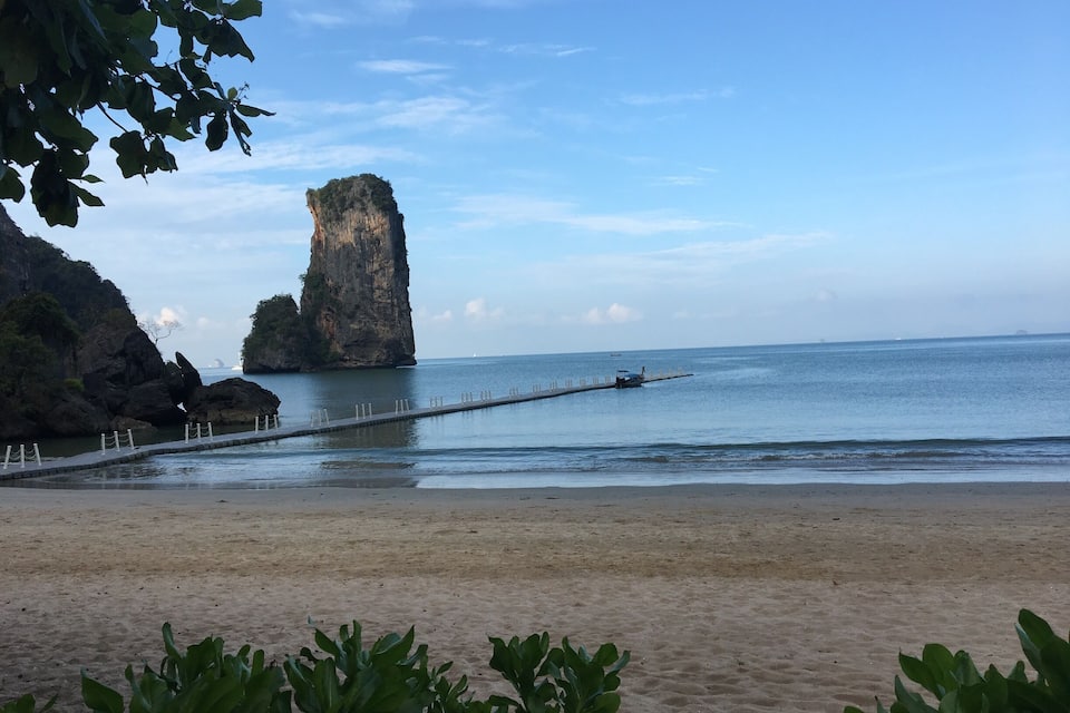 A beach with a prominent rock formation and a pier extending into the water.