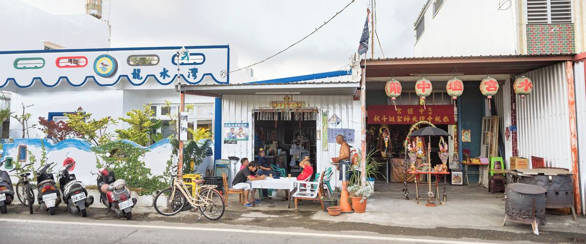 A street scene with a row of parked scooters, a small shop with a signboard, and a building with a tiled facade.