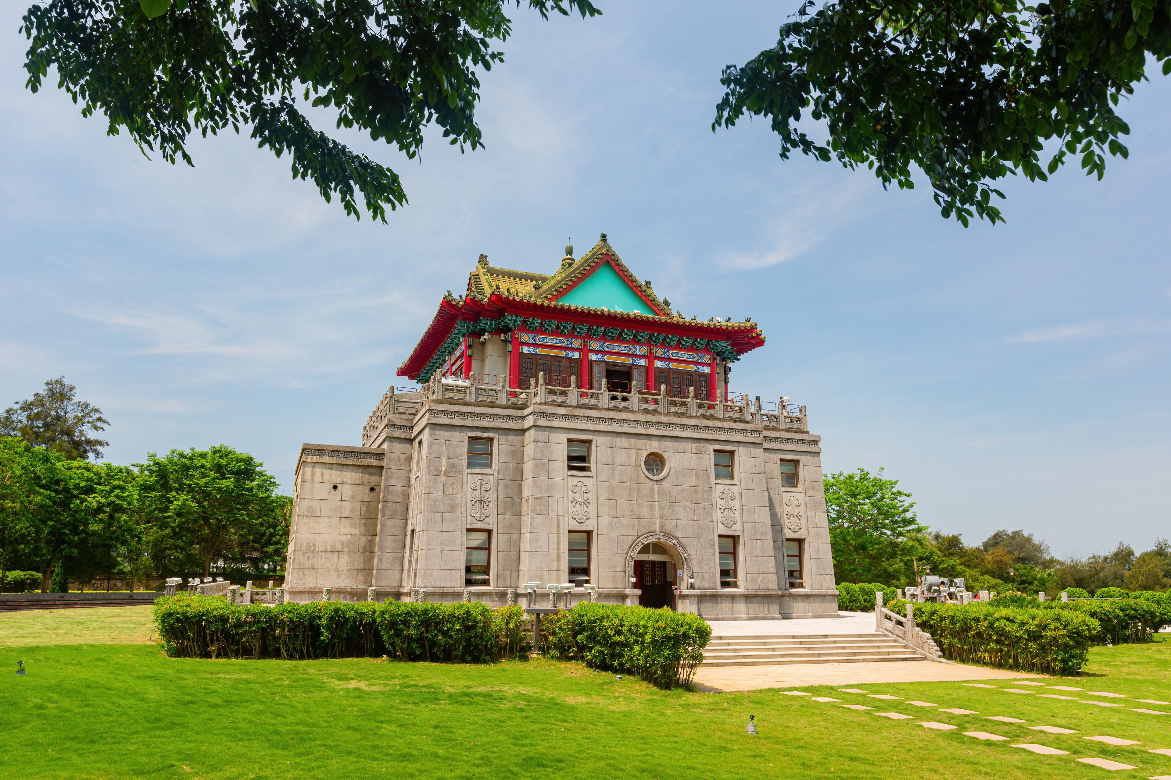 A traditional building with a green roof and red accents, surrounded by well-maintained grass and trees.