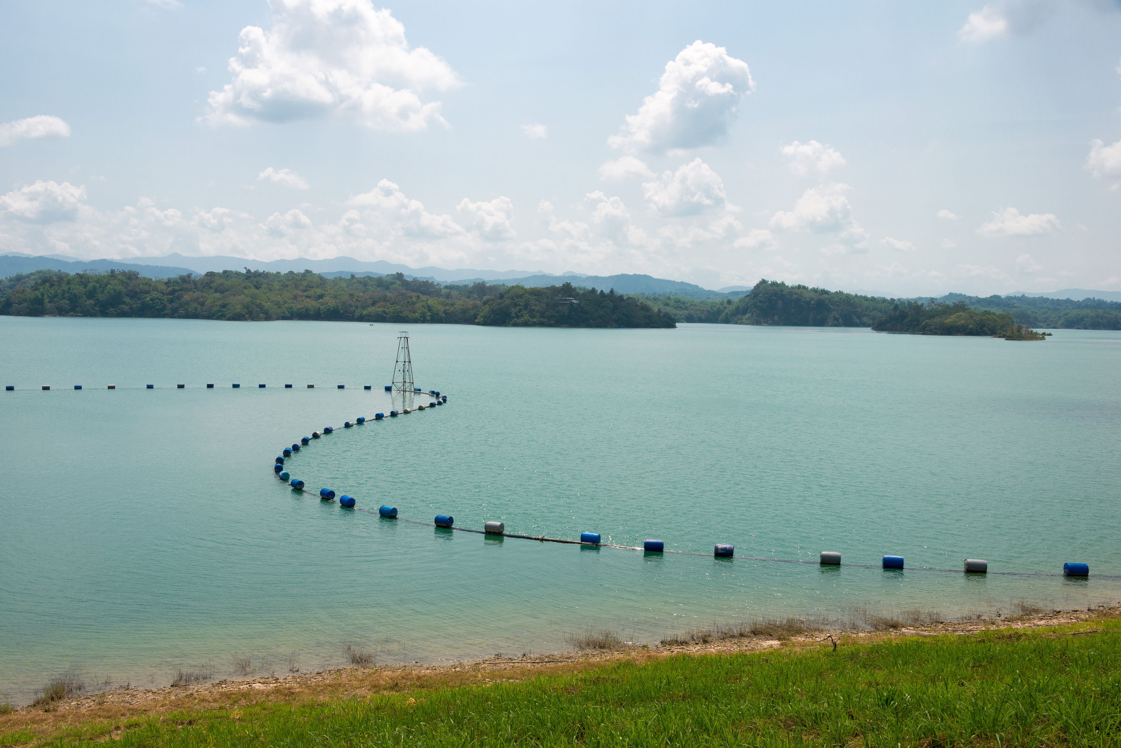A calm lake with a series of floating barriers and a distant shoreline.