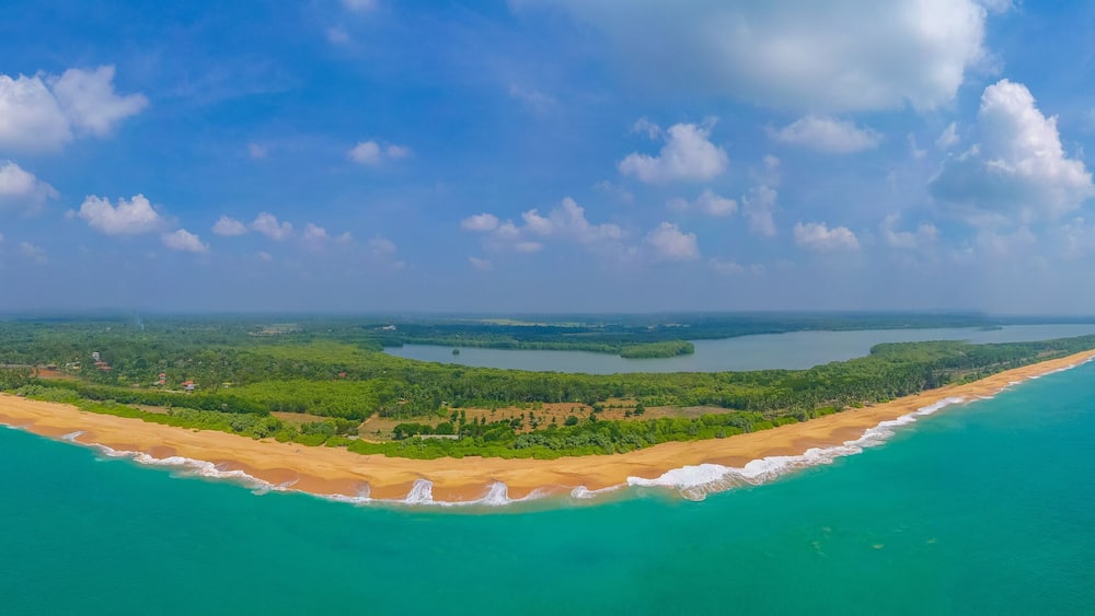A coastal landscape with a sandy beach, turquoise waters, and a forested island.