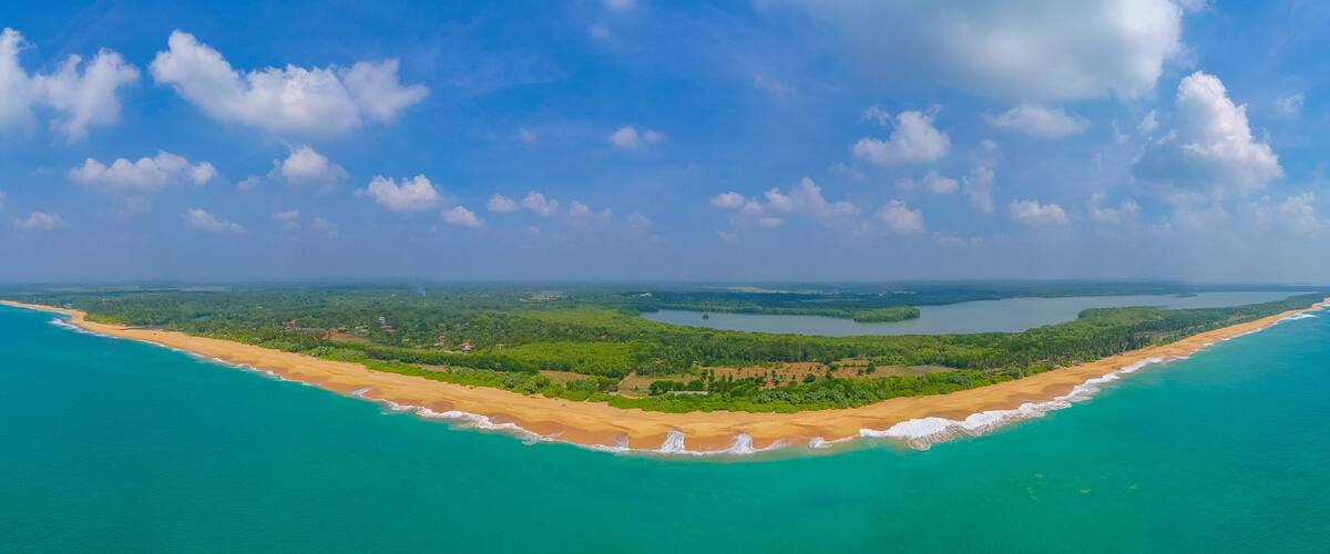 Eine Küstenlandschaft mit Sandstrand, türkisfarbenem Wasser und einer bewaldeten Insel.