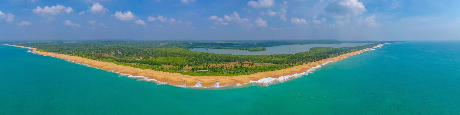 A coastal landscape with a sandy beach, turquoise waters, and a forested island.