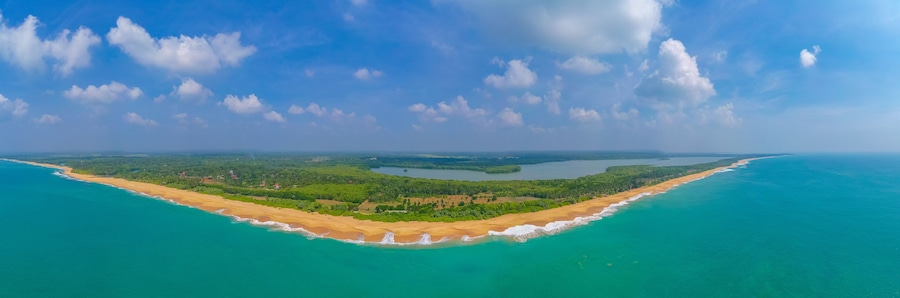 Eine Küstenlandschaft mit Sandstrand, türkisfarbenem Wasser und einer bewaldeten Insel.