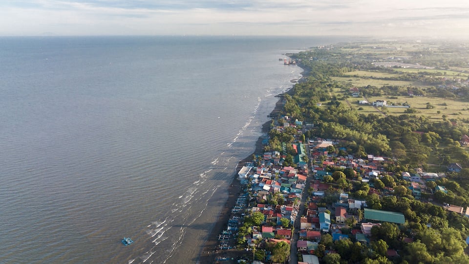 An aerial view of a coastal town with a beach, houses, and greenery.