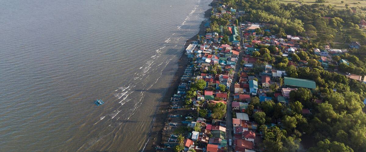 An aerial view of a coastal town with a beach, houses, and greenery.