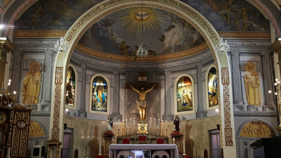 An ornate church interior with a crucifix, altar, and religious paintings.