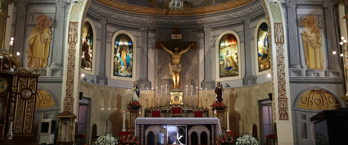 An ornate church interior with a crucifix, altar, and religious paintings.