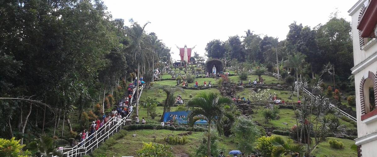 A hill with a statue at the top, surrounded by lush greenery and a white fence.