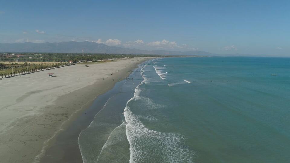 A beach with clear turquoise waters, a sandy shore, and distant mountains.