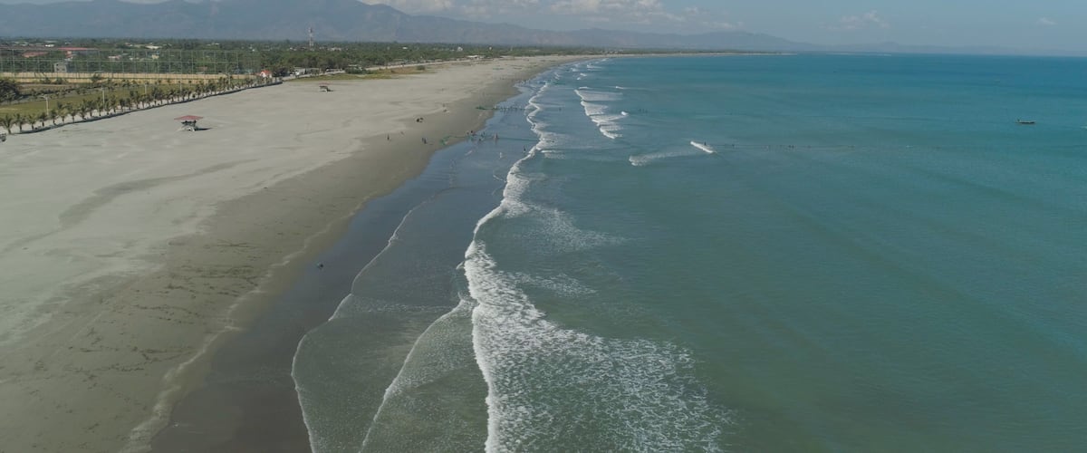 A beach with clear turquoise waters, a sandy shore, and distant mountains.