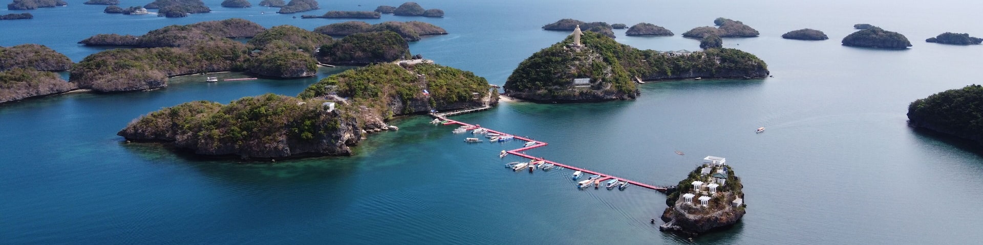 Aerial of Pilgrimage and Ramos Island, part of Hundred Islands in Alaminos, Pangasinan, Philippines. Visible is a red floating deck with many boats.