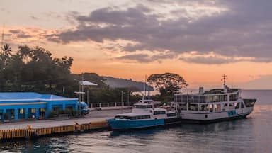 Un puerto con dos barcos amarrados, un edificio azul y un cielo al atardecer.
