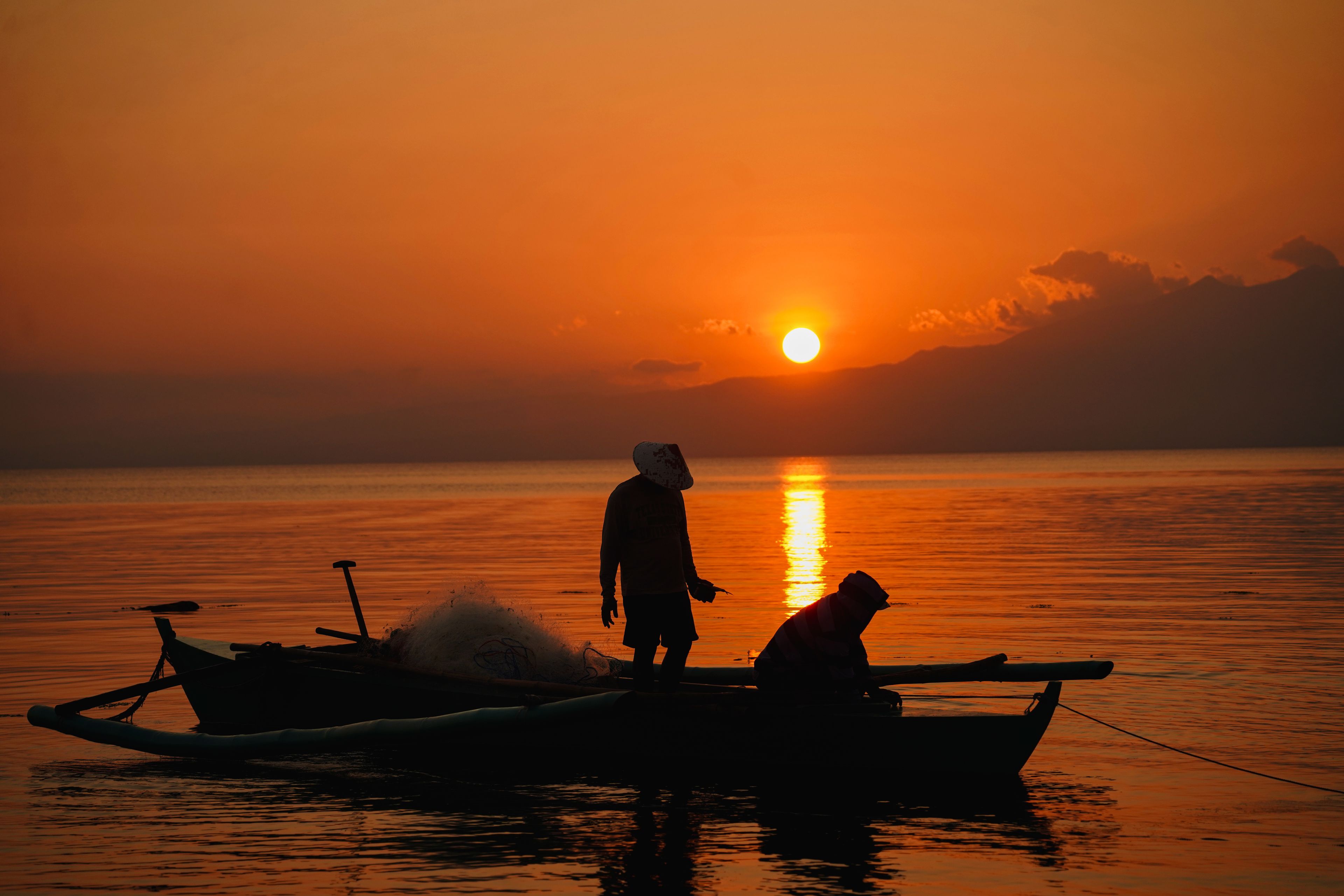 A sunset over a calm body of water with a person standing on a boat.