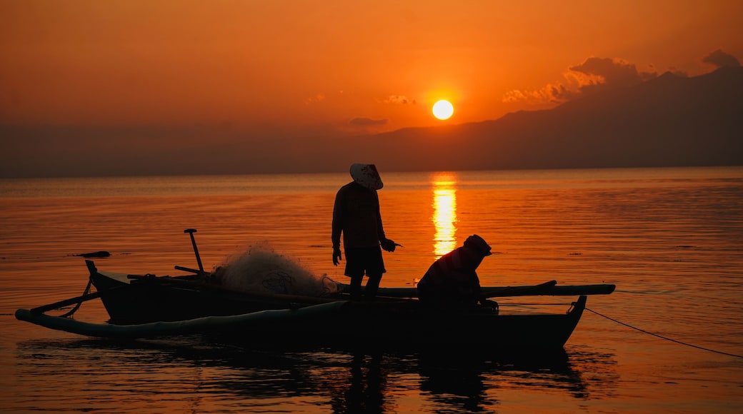 A sunset over a calm body of water with a person standing on a boat.