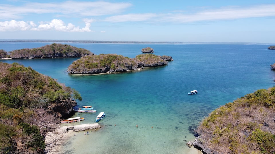 A coastal area with clear turquoise waters, rocky islands, and boats anchored near the shore.