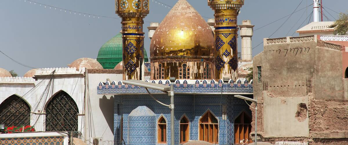 A mosque with two minarets, a golden dome, and a green dome.