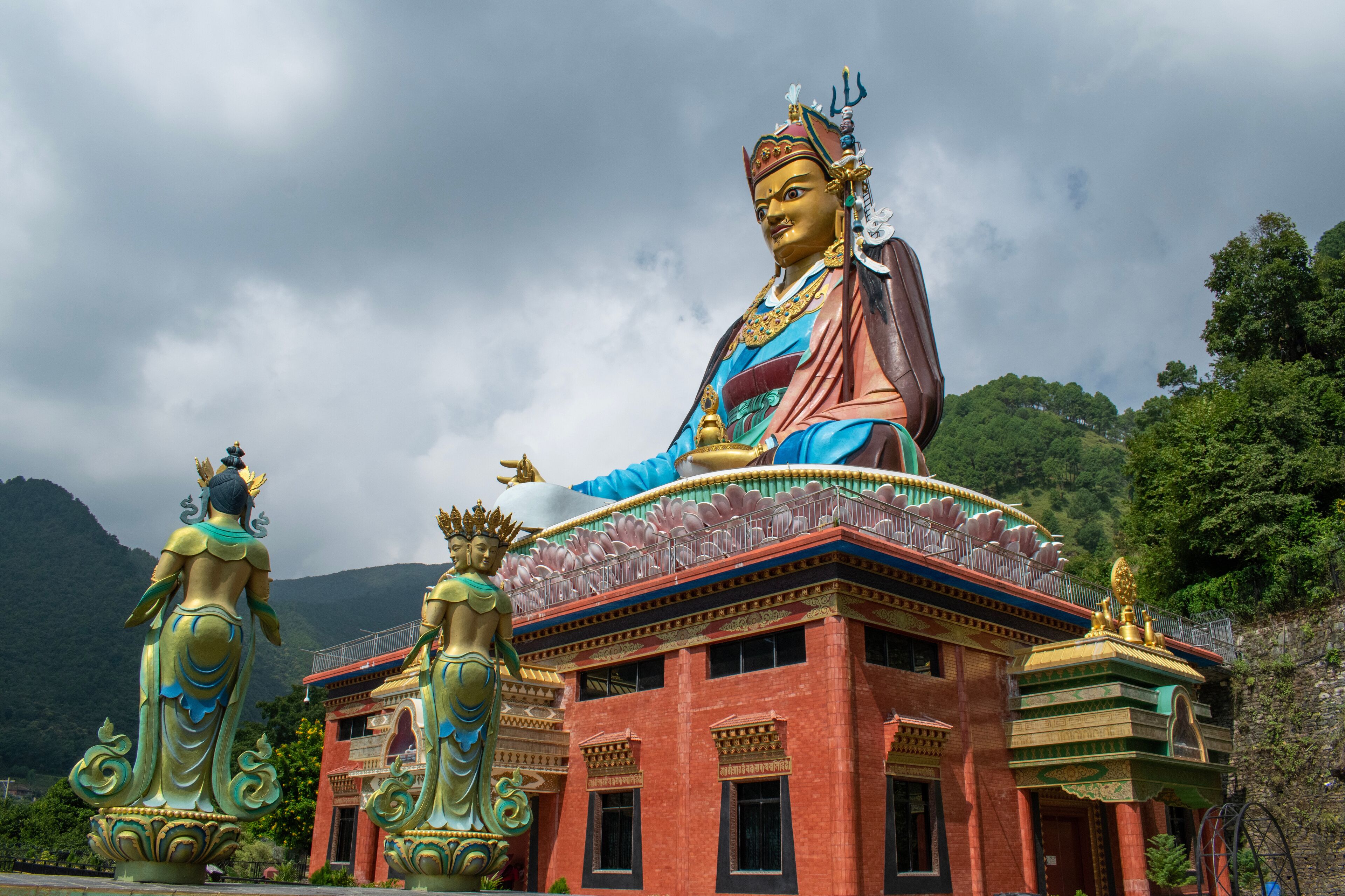A large statue of a deity with a blue robe and golden jewelry, set against a mountainous backdrop.