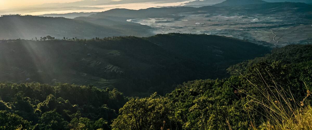 A mountainous landscape with a river valley and distant mountains under a clear sky.