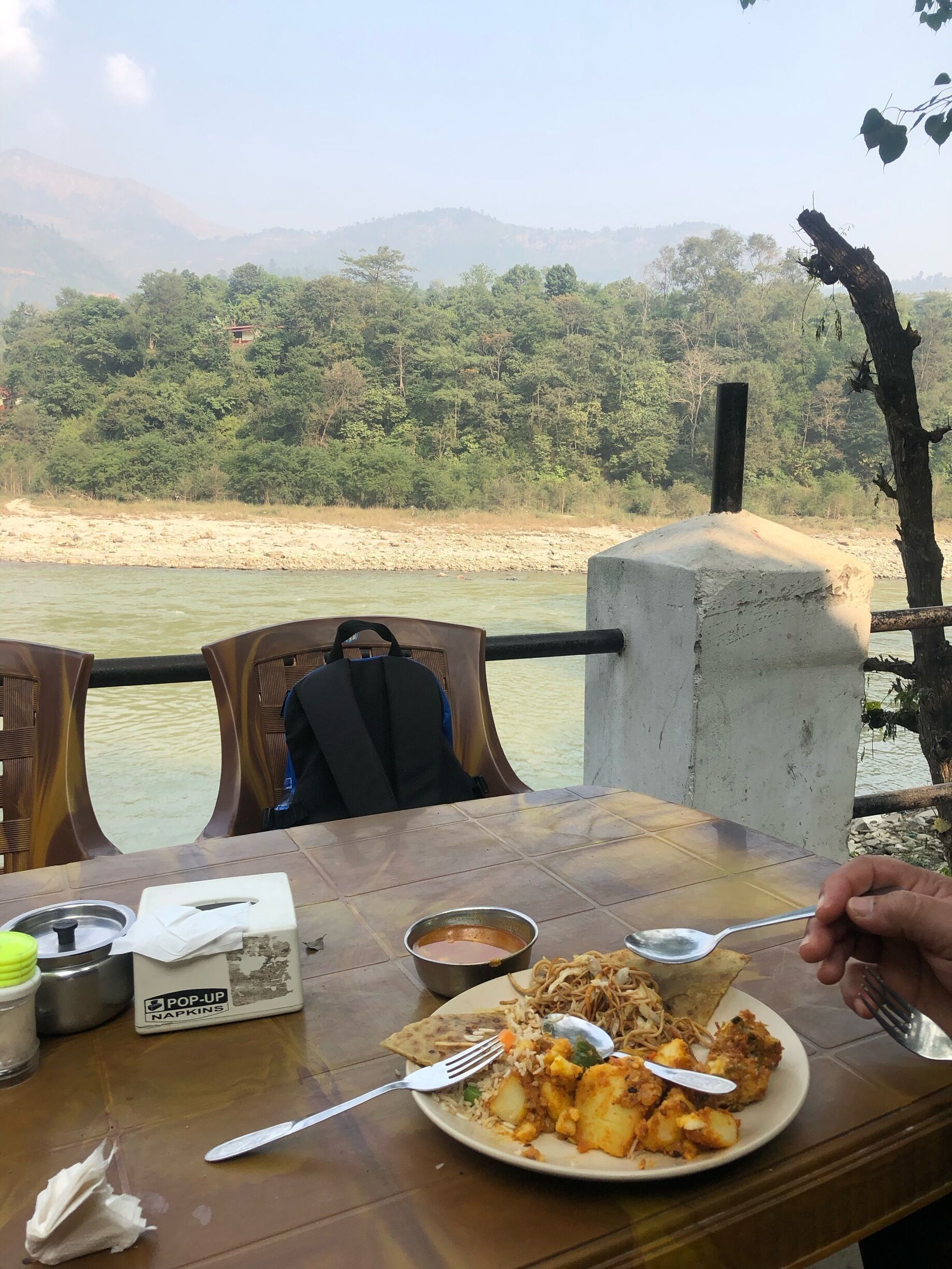 A dining table with a meal, a river, and a forested hillside in the background.