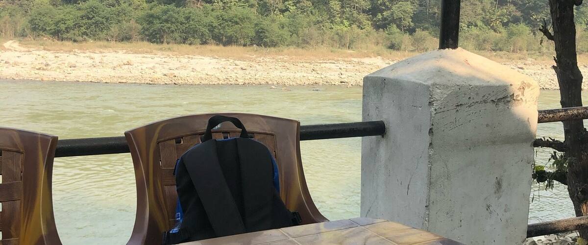 A dining table with a meal, a river, and a forested hillside in the background.