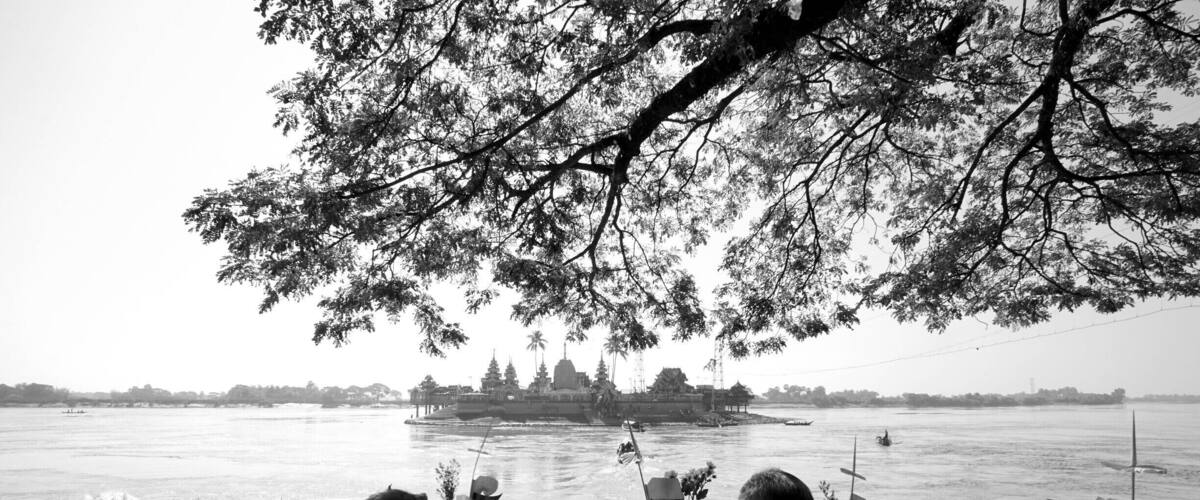 A river with boats, a crowd of people, and a temple in the background.