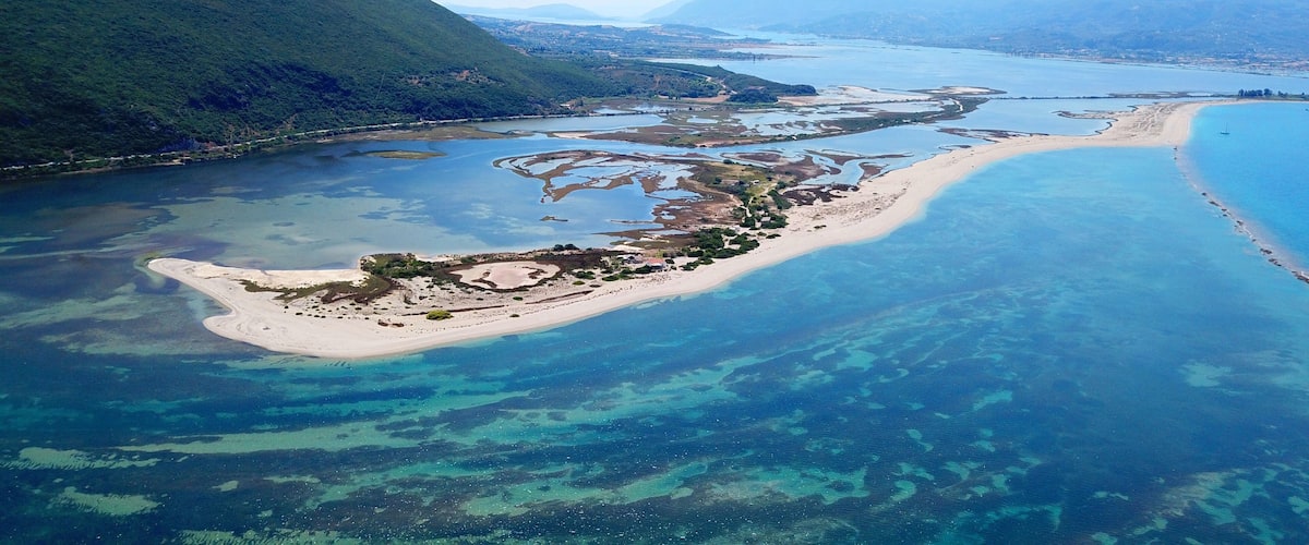 A coastal landscape with a sandy beach, clear blue waters, and a mountainous backdrop.