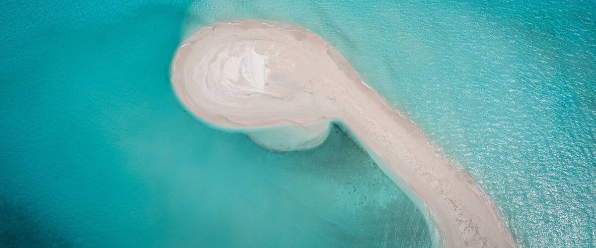 An aerial view of a crescent-shaped sandy beach with clear turquoise waters.