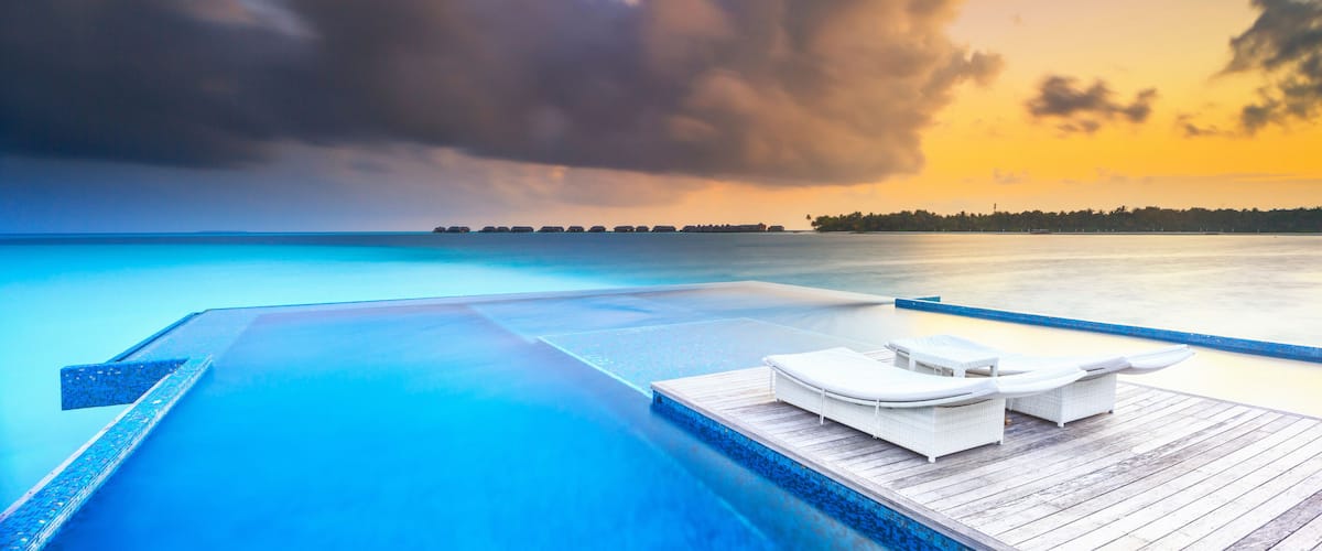 A poolside with lounge chairs and a wooden deck overlooking a calm sea.