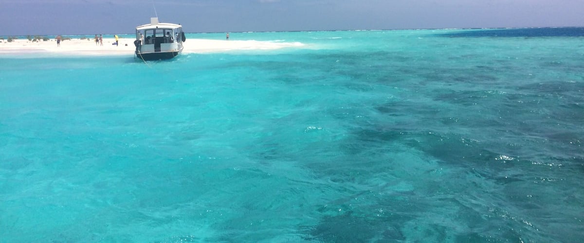 A boat on turquoise waters near a sandy beach.