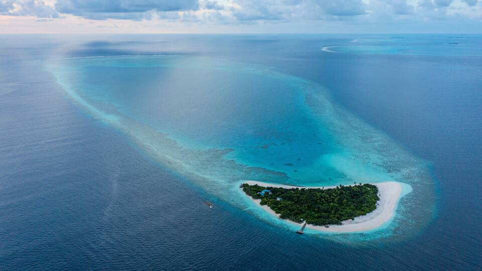 An aerial view of a turquoise atoll with clear waters and a small island with dense vegetation.