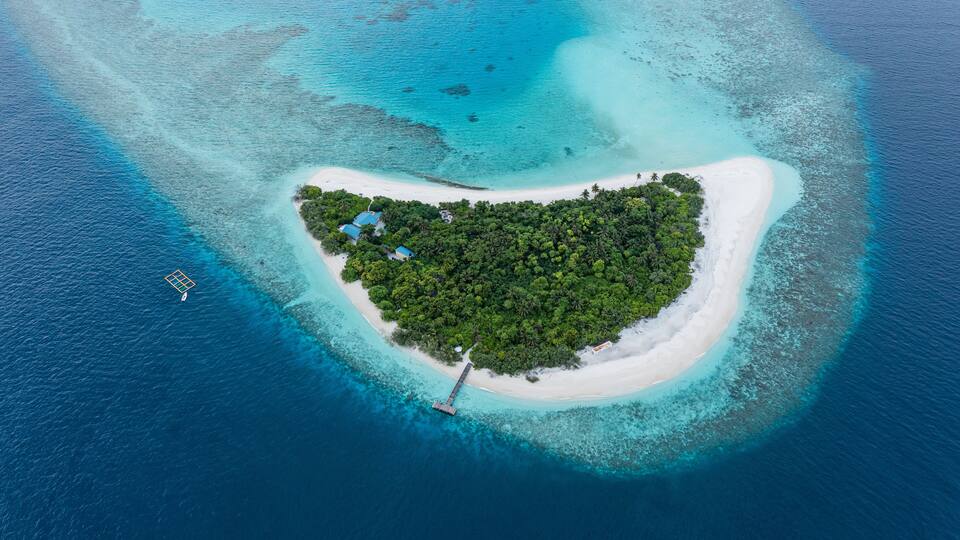 An aerial view of a small, lush island surrounded by turquoise waters.