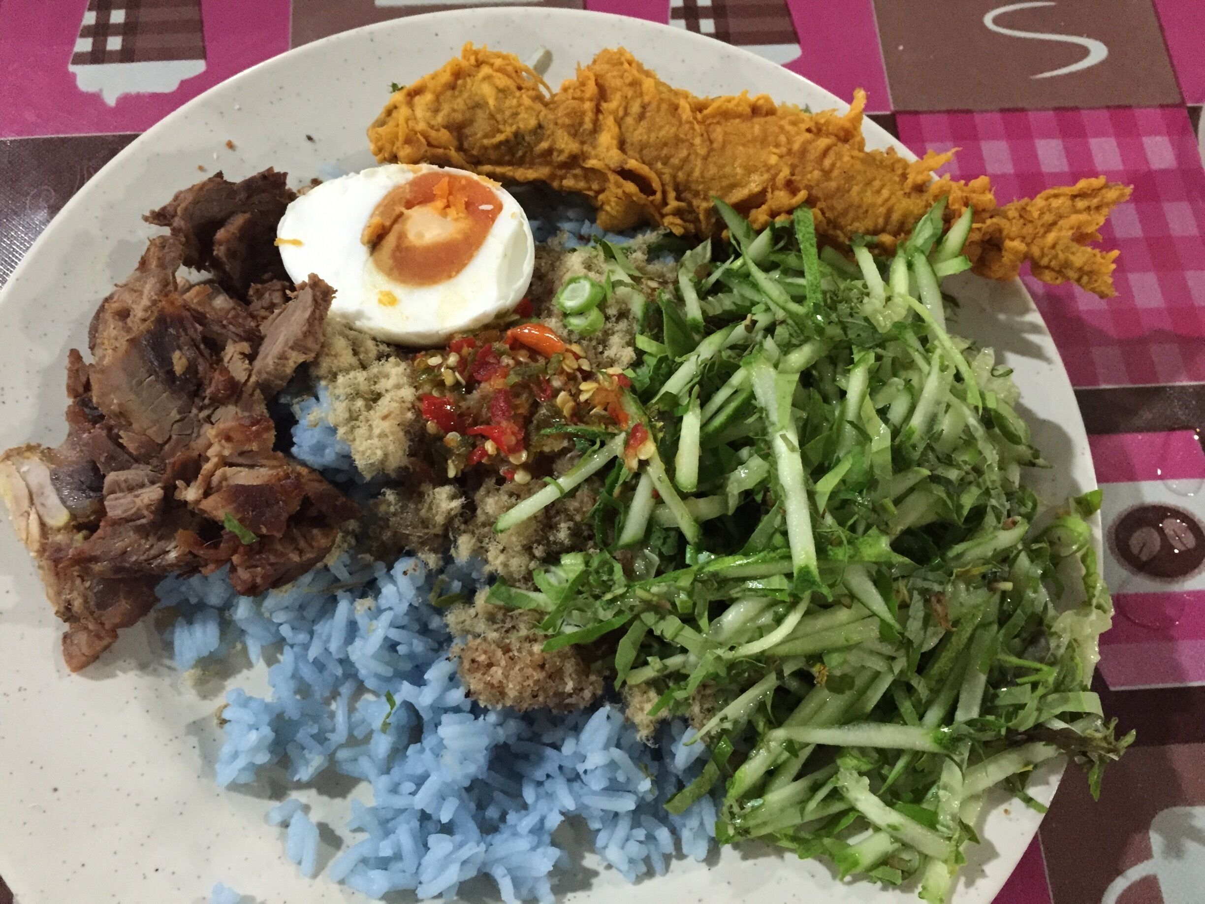 A plate of food with blue rice, fried chicken, a boiled egg, and a salad.