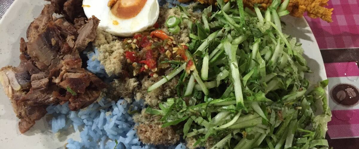 A plate of food with blue rice, fried chicken, a boiled egg, and a salad.