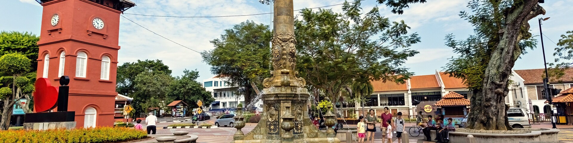 Una fuente histórica con una torre de reloj y un árbol grande en una plaza pública.
