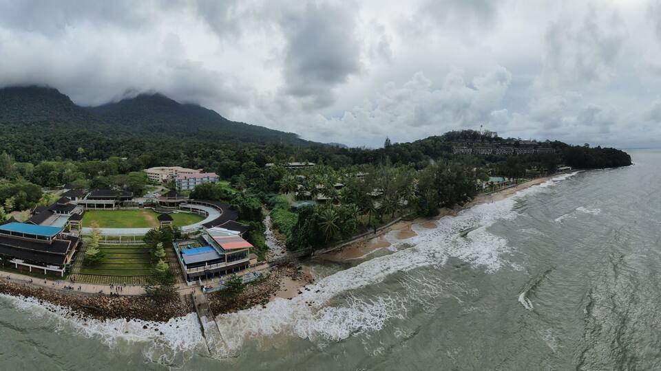 A coastal town with a beach, buildings, and a mountainous backdrop.