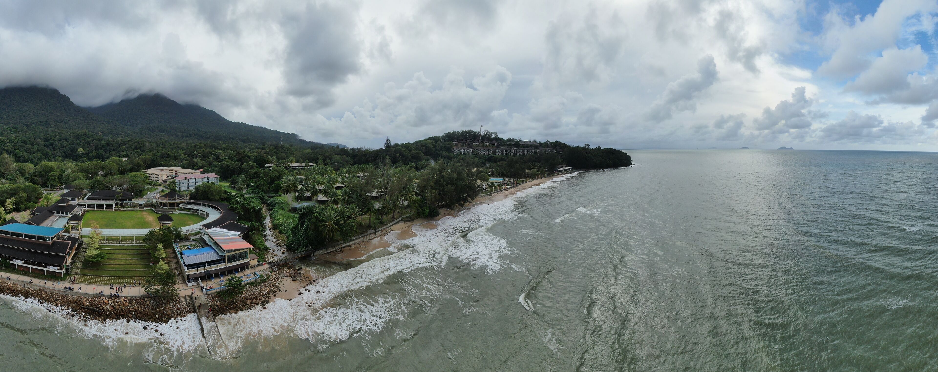A coastal town with a beach, buildings, and a mountainous backdrop.