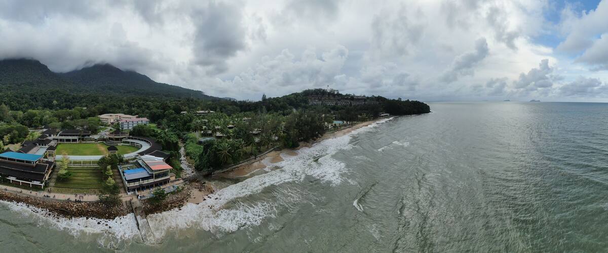 A coastal town with a beach, buildings, and a mountainous backdrop.