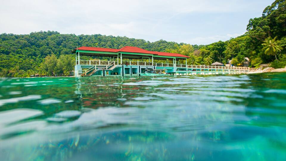 A turquoise lagoon with a floating structure featuring a red roof and blue walls.