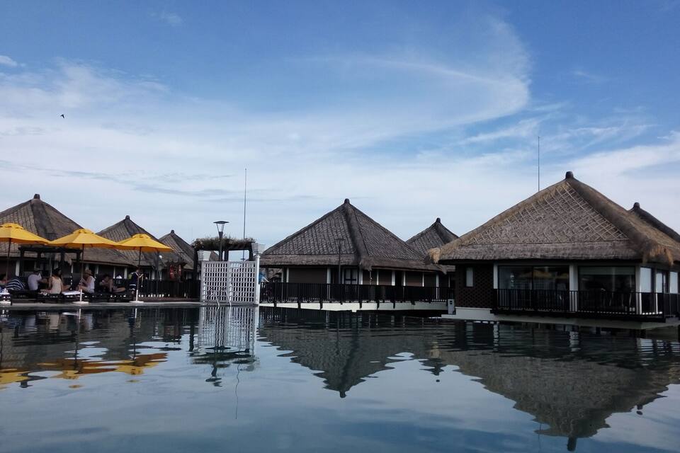 Overwater bungalows with thatched roofs, a pool, and a waterfall.