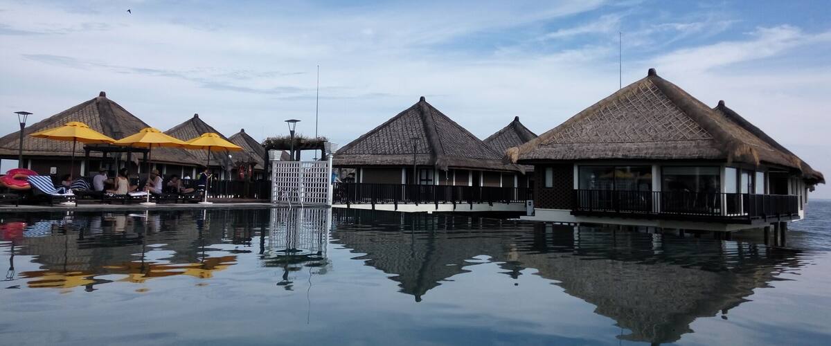 Overwater bungalows with thatched roofs, a pool, and a waterfall.